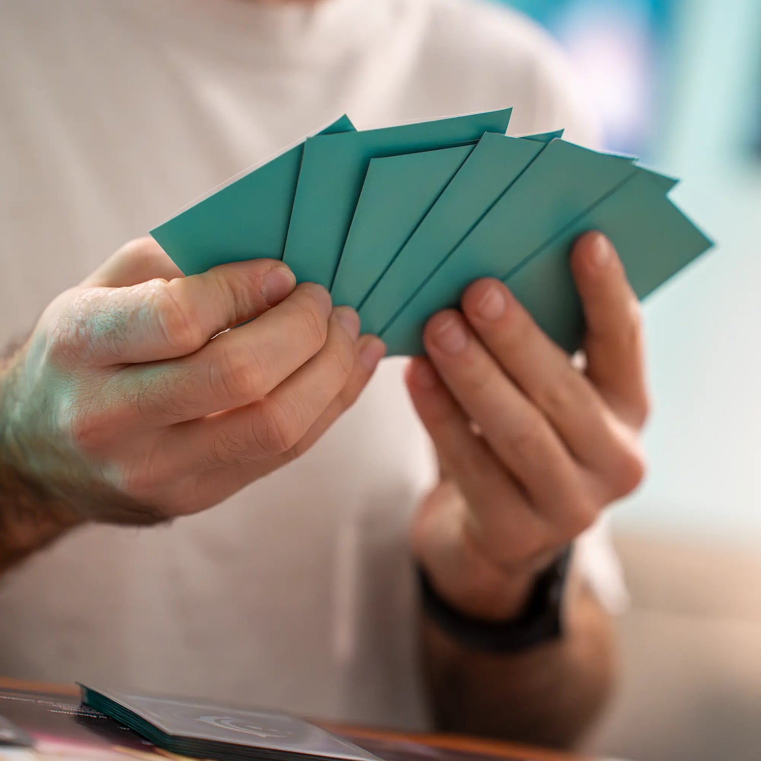 hands holding multiple turquoise matte textured dual reef sleeves with black inside and clear front for standard size tcg trading cards